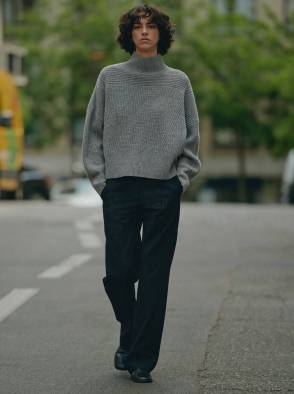 Woman in a white patterned dress standing outdoors in a sunlit street with a pink building in the background.