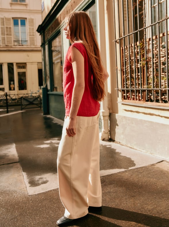 Woman in a white patterned dress standing outdoors in a sunlit street with a pink building in the background.